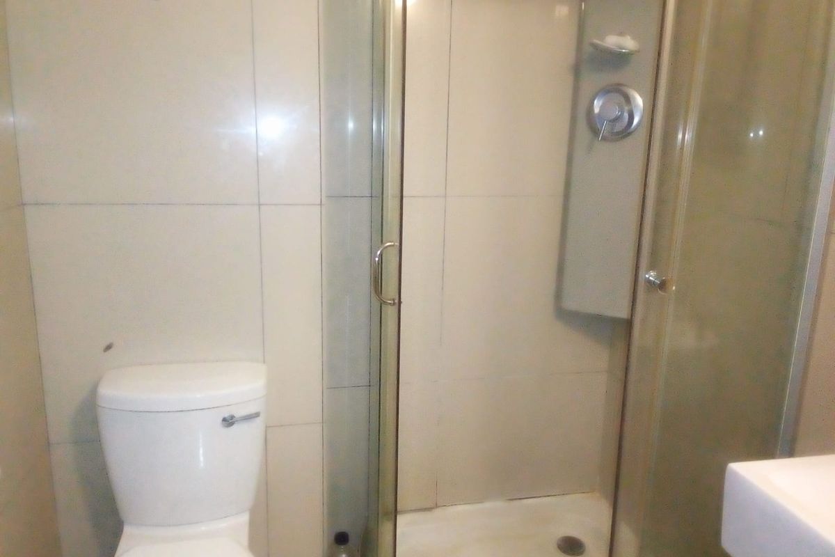 A functional bathroom featuring a glass-enclosed shower, toilet, and vanity basin with neutral wall tiling.