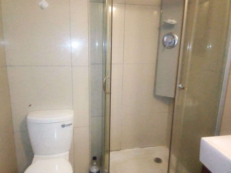 A functional bathroom featuring a glass-enclosed shower, toilet, and vanity basin with neutral wall tiling.