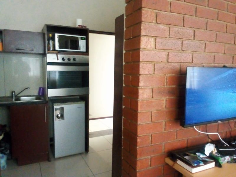 Open plan living area featuring a compact kitchen with built-in oven and microwave, complemented by an exposed brick feature wall.