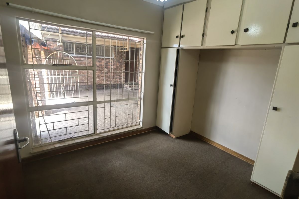 A vacant bedroom featuring built-in cupboards, carpeted flooring, and large windows fitted with security bars.