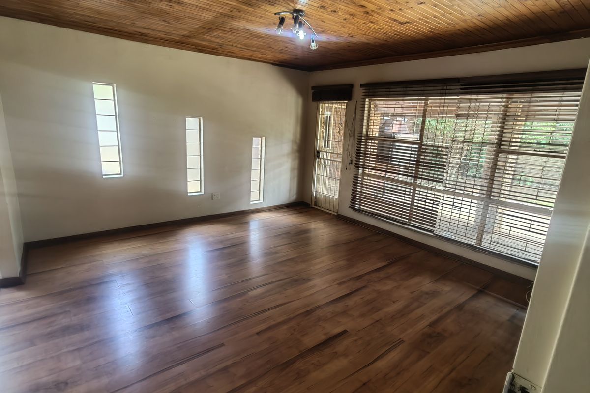 Spacious living area featuring warm timber ceilings, laminate flooring, and natural light through multiple windows with fitted blinds and a security gate.