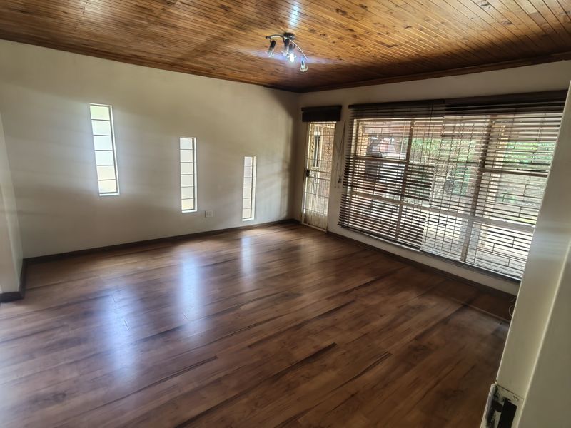 Spacious living area featuring warm timber ceilings, laminate flooring, and natural light through multiple windows with fitted blinds and a security gate.