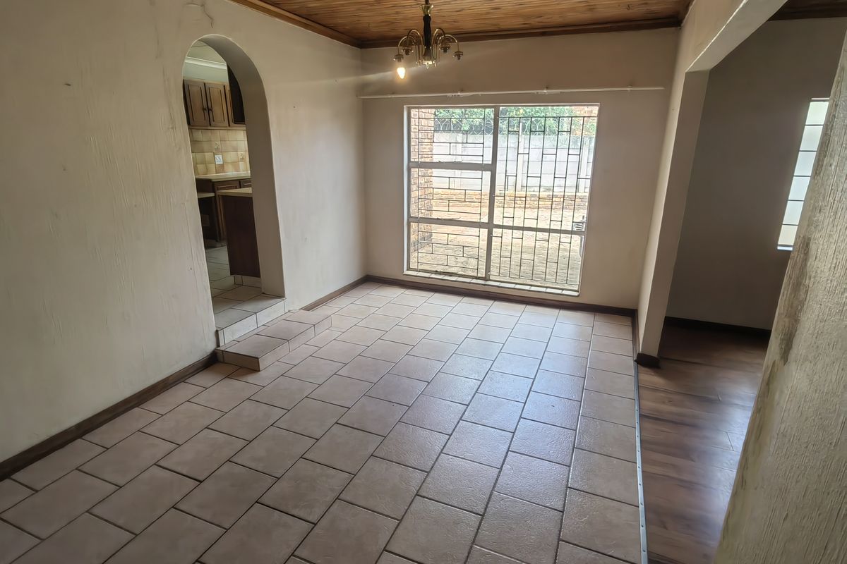 An empty living room featuring tiled floors, a timber ceiling, and an arched doorway leading to the kitchen area.