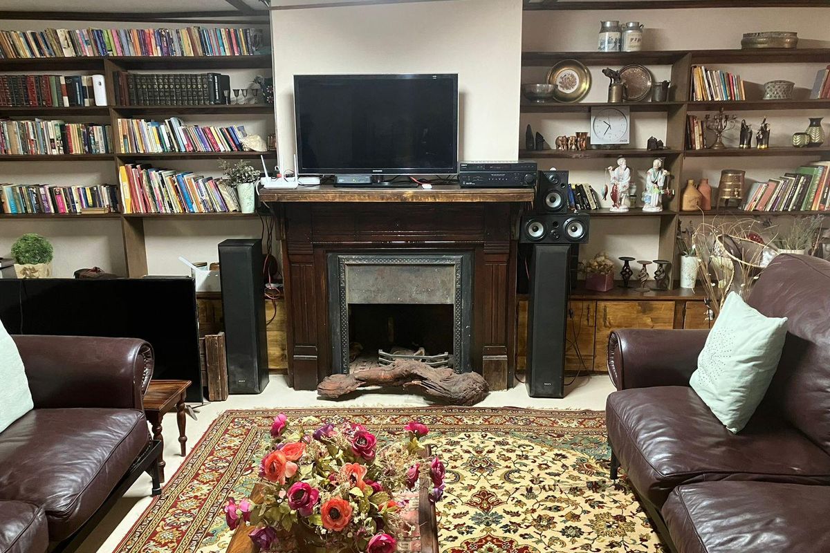A cozy living room featuring a prominent dark wood fireplace mantel and extensive built-in floor-to-ceiling wooden shelving units.