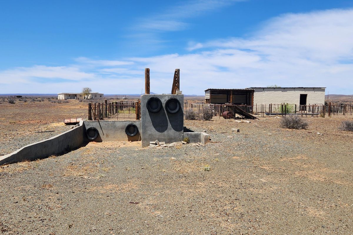 An exterior view of a farm property featuring a concrete livestock loading ramp, perimeter fencing, and a small outbuilding in a rural landscape.