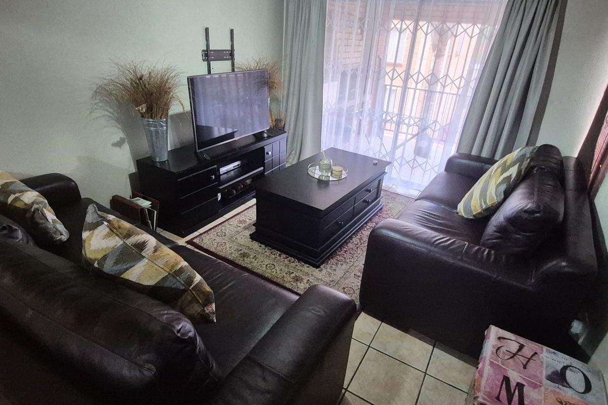 A comfortable living room featuring tiled flooring and a sliding glass door with an integrated security gate, providing access to the exterior.