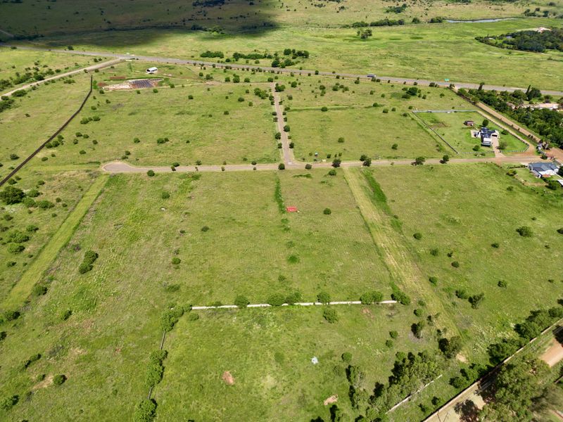 An aerial view of a large, vacant residential plot featuring natural vegetation, perimeter fencing, and direct access to a paved road.
