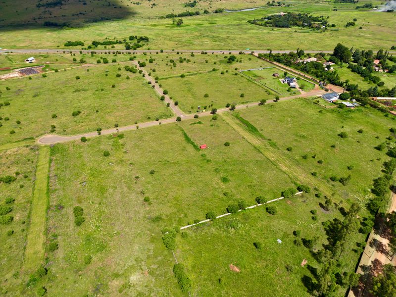 An aerial view of a large, undeveloped residential land parcel featuring established road access and surrounding green landscape.
