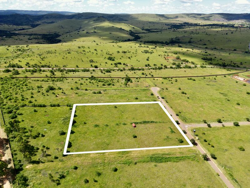 An aerial view of a vacant residential plot of land situated in a scenic, open landscape with established road access.