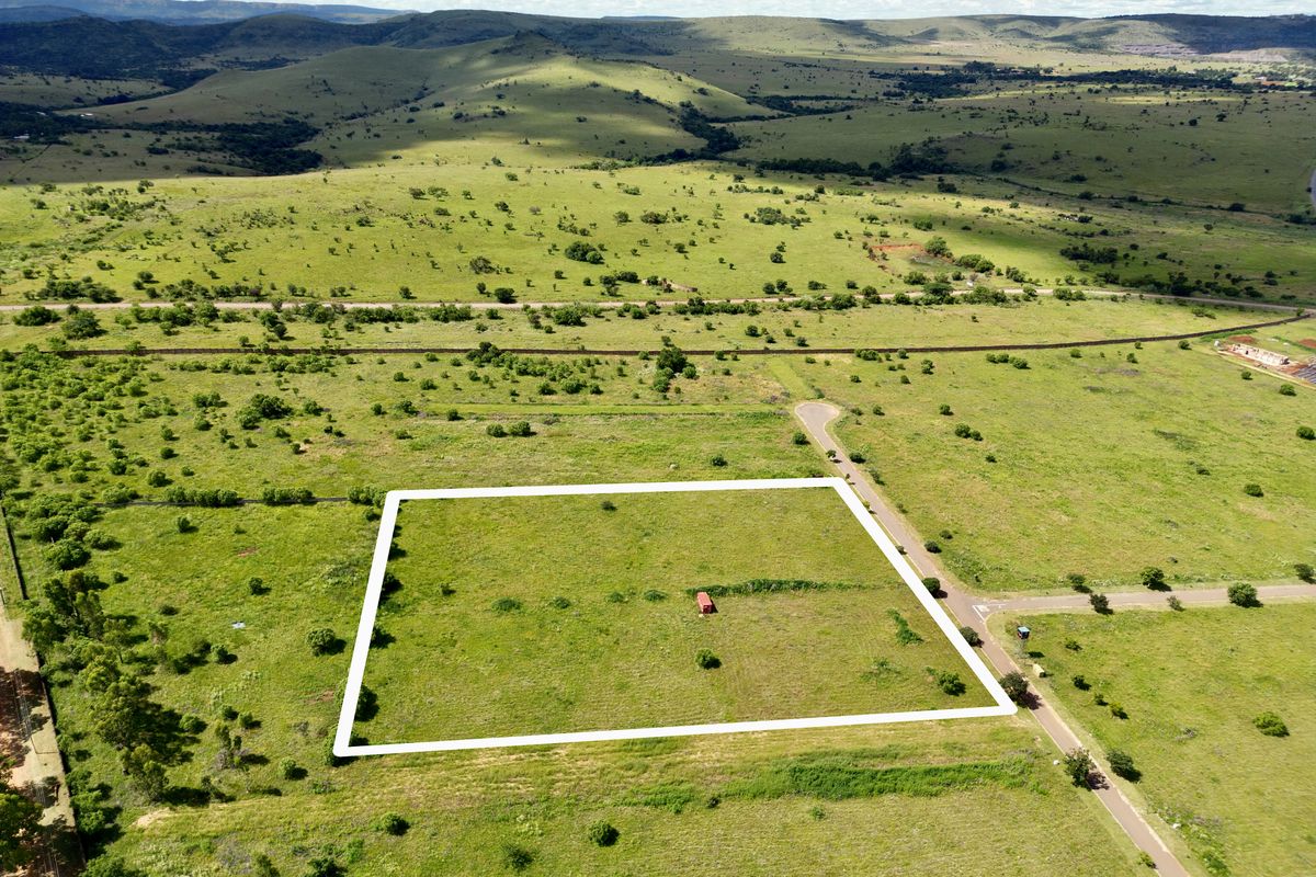 An aerial view of a vacant residential plot of land situated in a scenic, open landscape with established road access.