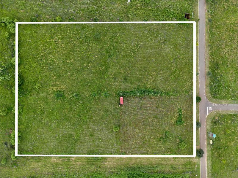 An aerial view of a vacant residential plot of land, featuring open green space and clear boundary lines.