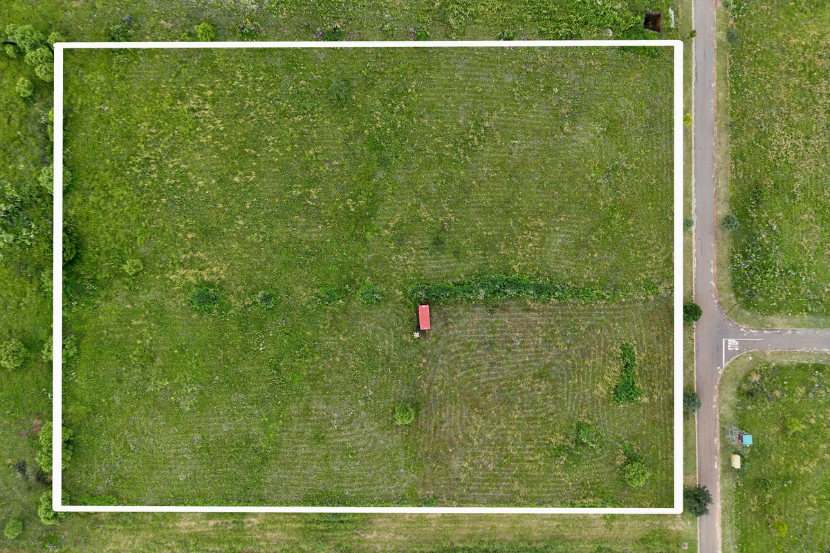 An aerial view of a vacant residential plot of land, featuring open green space and clear boundary lines.