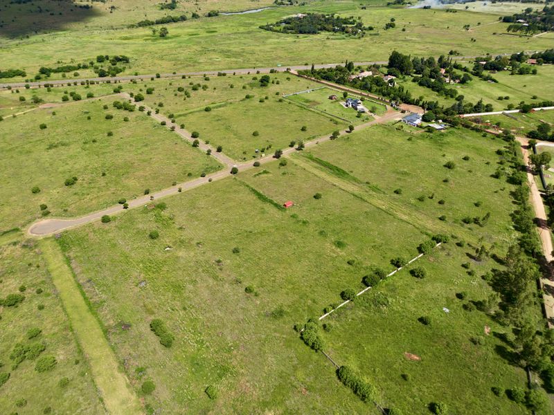 An aerial view of a residential vacant land plot featuring established paved road access and surrounding natural grassland landscape.