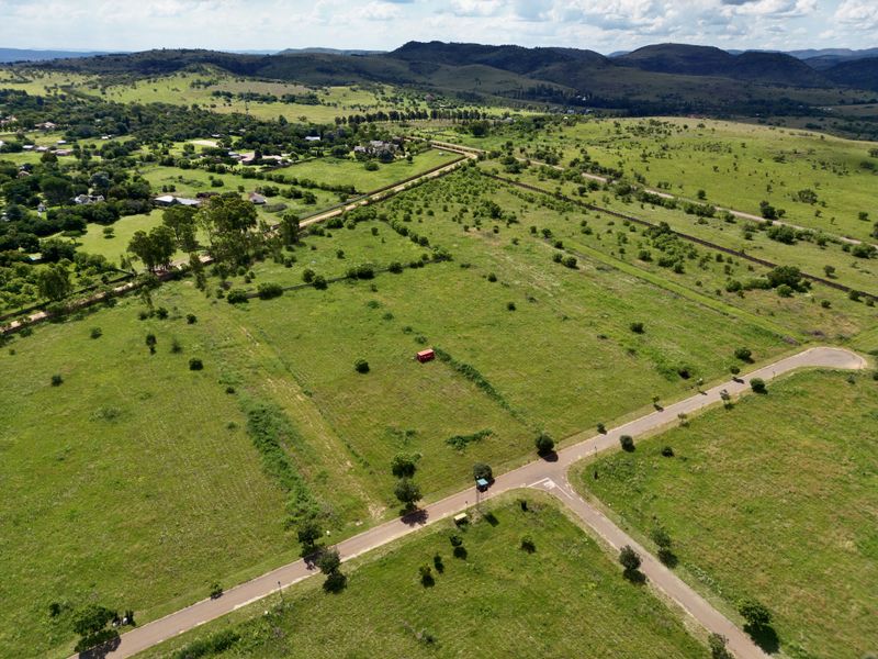 An aerial view of a large, undeveloped residential land plot featuring established road access and surrounding natural landscape.