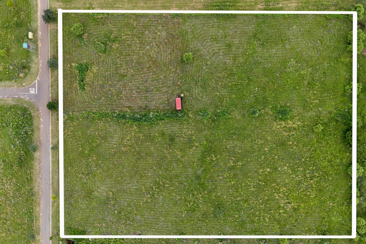 An aerial view of a vacant residential plot of land, featuring open grass coverage and direct access to the adjacent road.