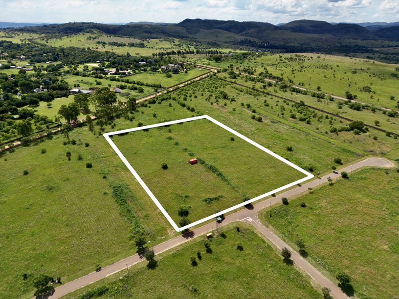 Aerial view of a vacant residential plot featuring clear boundary lines, situated in a scenic landscape with established road access.