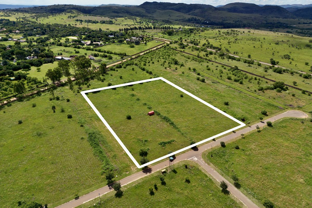 Aerial view of a vacant residential plot featuring clear boundary lines, situated in a scenic landscape with established road access.