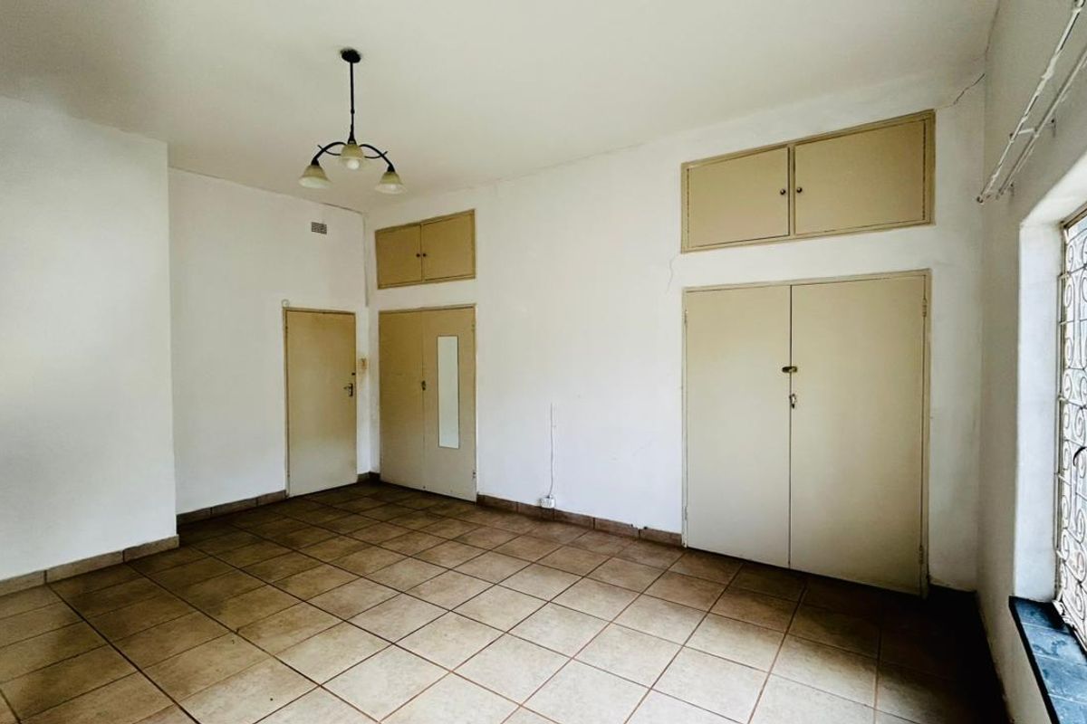 An empty bedroom featuring tiled flooring, built-in cupboards, and overhead storage cabinets, with security bars installed on the window.