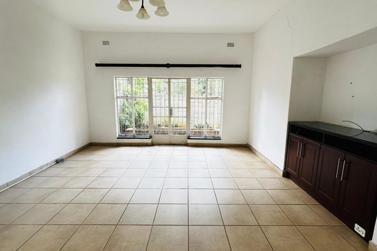 An empty living room featuring tiled flooring, built-in cabinetry, and a security gate leading to the exterior.