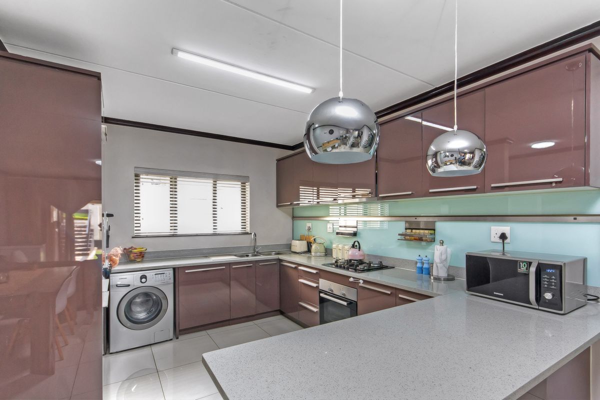 Modern kitchen featuring high-gloss cabinetry, stone countertops, integrated gas hob, built-in oven, and dedicated space for a washing machine.