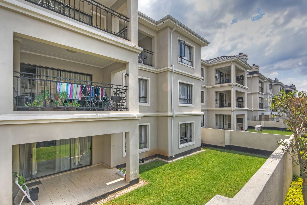 Exterior view of a multi-story apartment complex featuring private balconies with wrought iron railings, tiled patio areas, and a shared garden space.