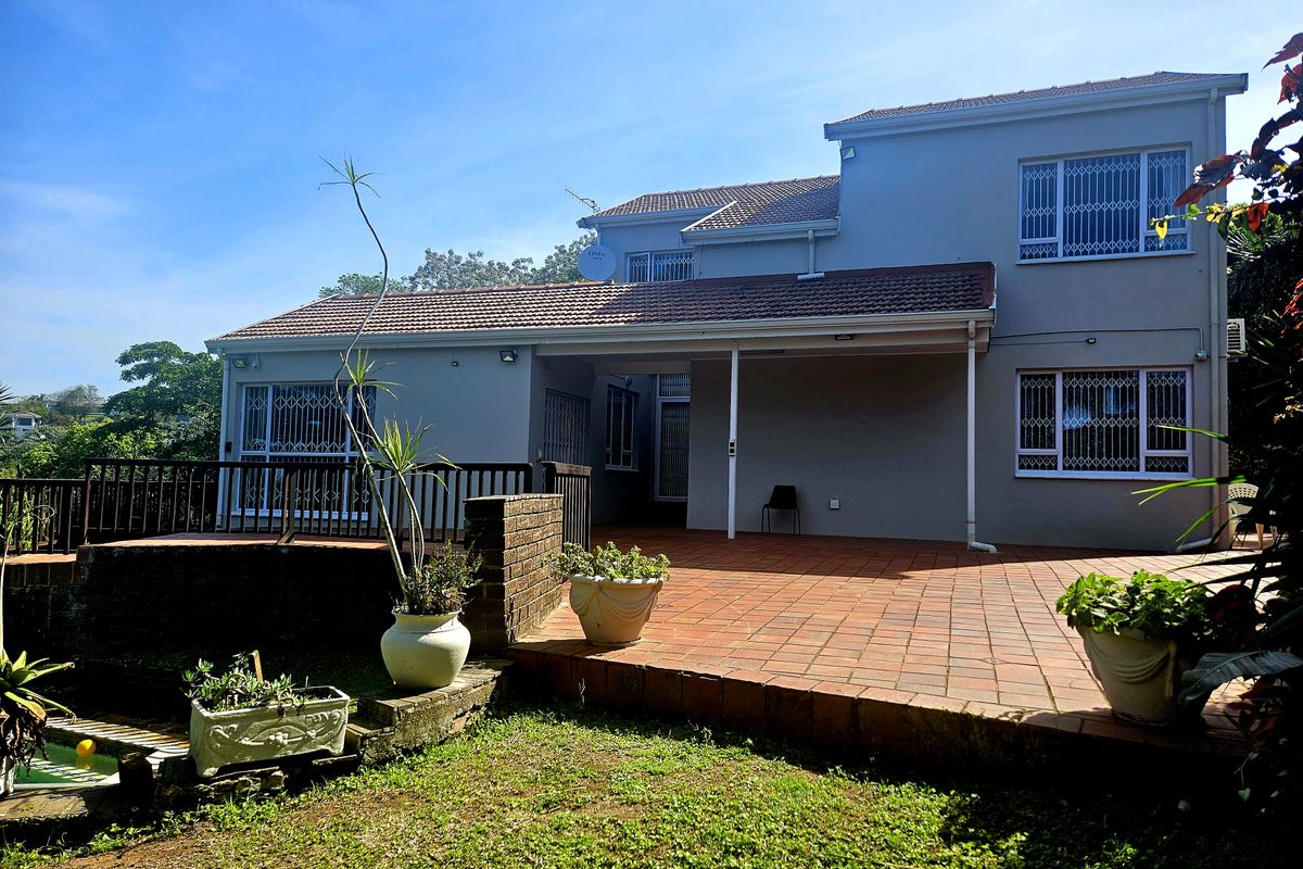 Rear view of a two-story house featuring a spacious tiled patio, security bars on windows, and a brick retaining wall overlooking the garden.