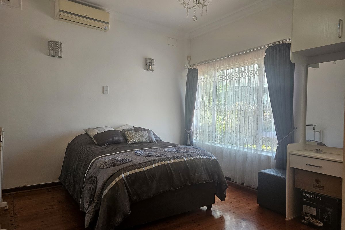 A bedroom featuring polished hardwood floors, a split-system air conditioner, built-in vanity, and a security gate on the window.