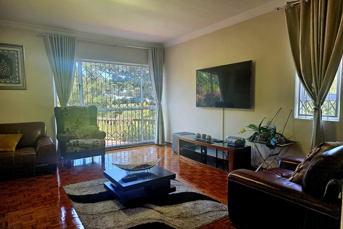 A comfortable living room featuring polished parquet flooring, large windows with security bars, and neutral wall finishes.