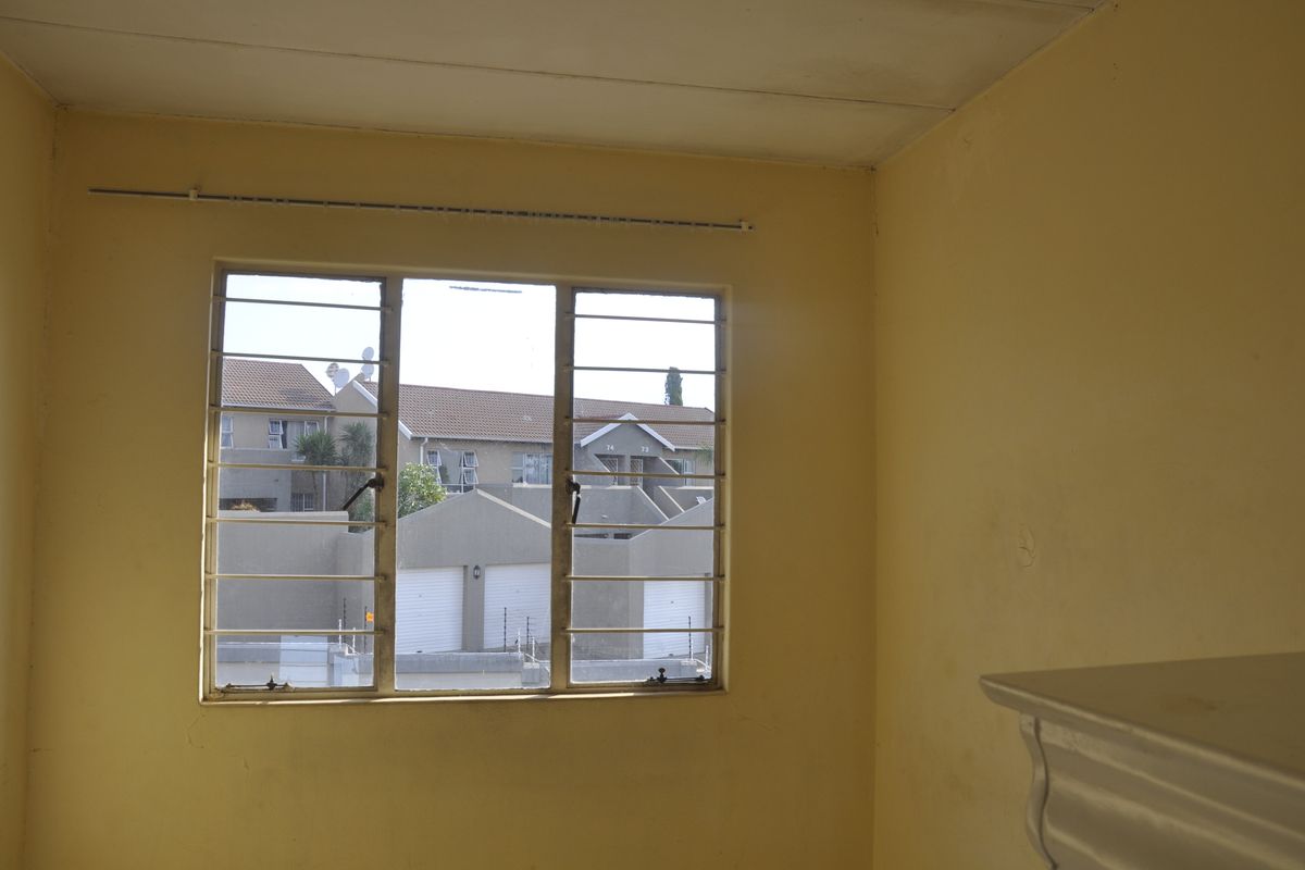 A vacant bedroom featuring yellow walls, a metal-framed window with security bars, and a view of the surrounding apartment complex.