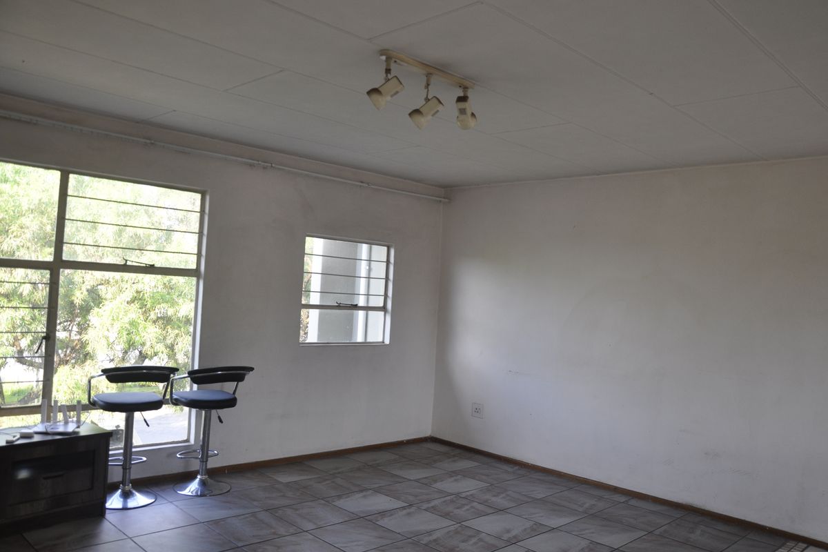 An empty living area featuring tiled flooring, large windows with security bars, and a ceiling-mounted spotlight fixture.