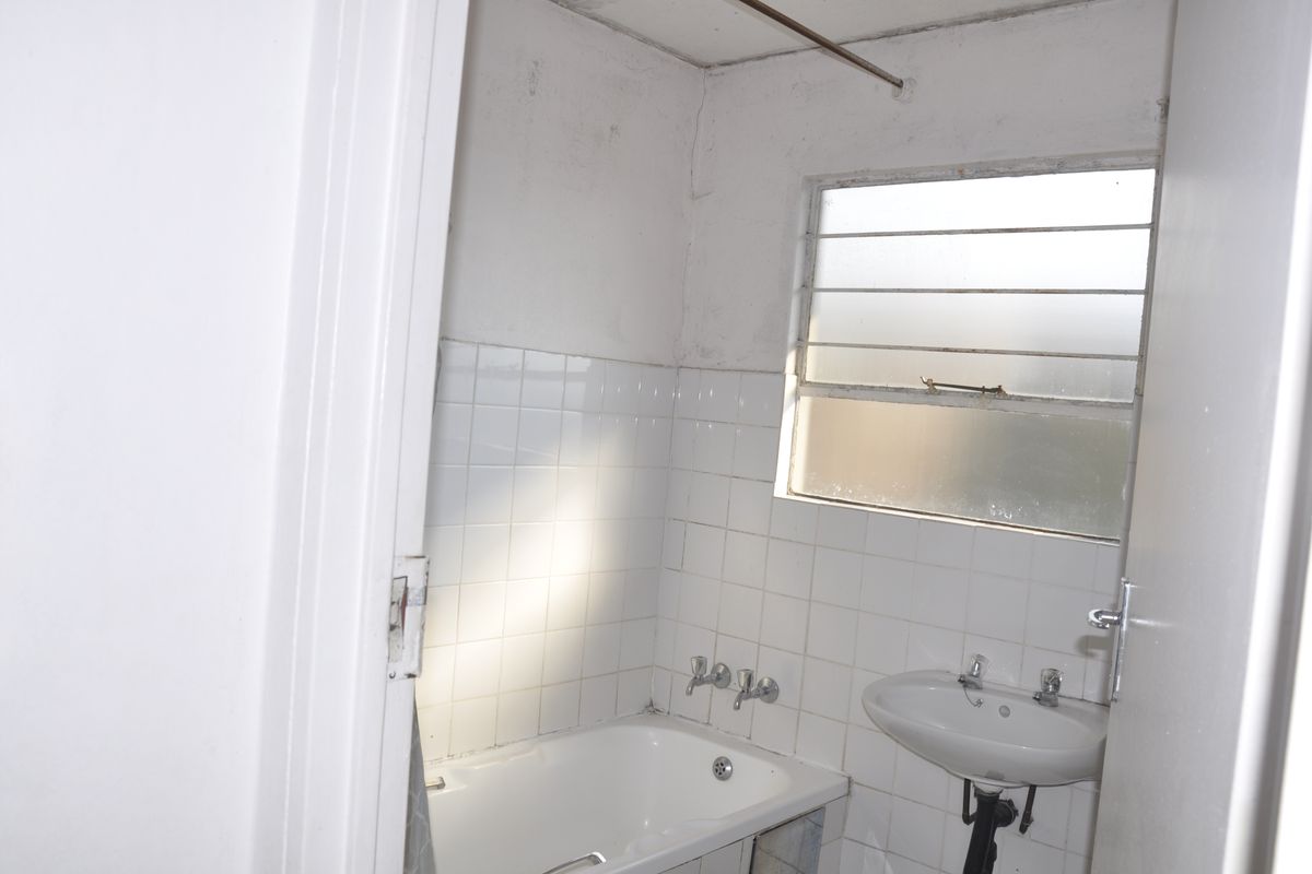 A dated bathroom featuring a standard bathtub, pedestal basin, and louvered window, requiring cosmetic updates and modernization of fixtures.