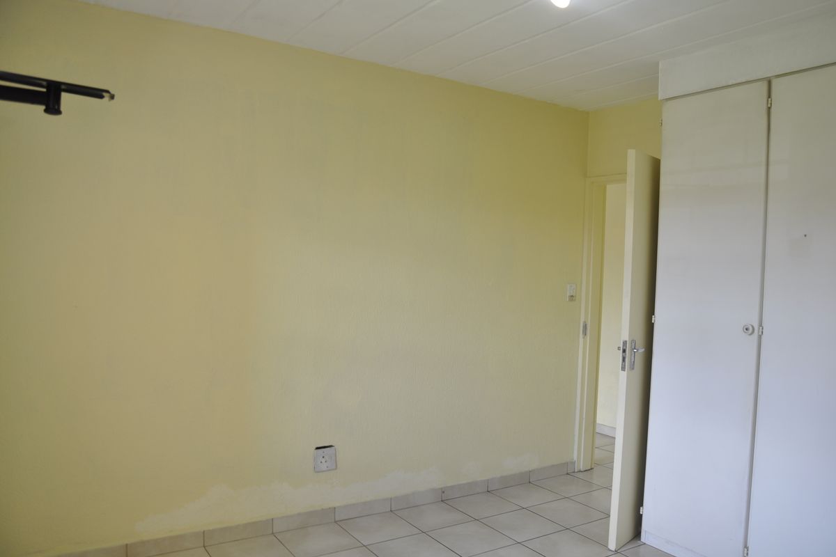 A vacant bedroom featuring tiled flooring, built-in cupboards, and a neutral yellow wall finish, ready for renovation or personalization.