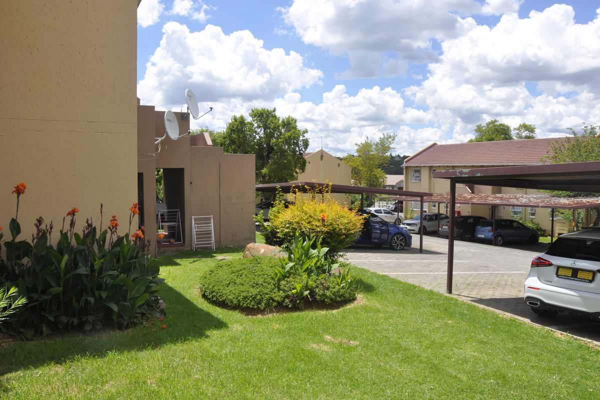 Exterior view of the apartment complex featuring landscaped garden beds, paved parking area, and covered carports.