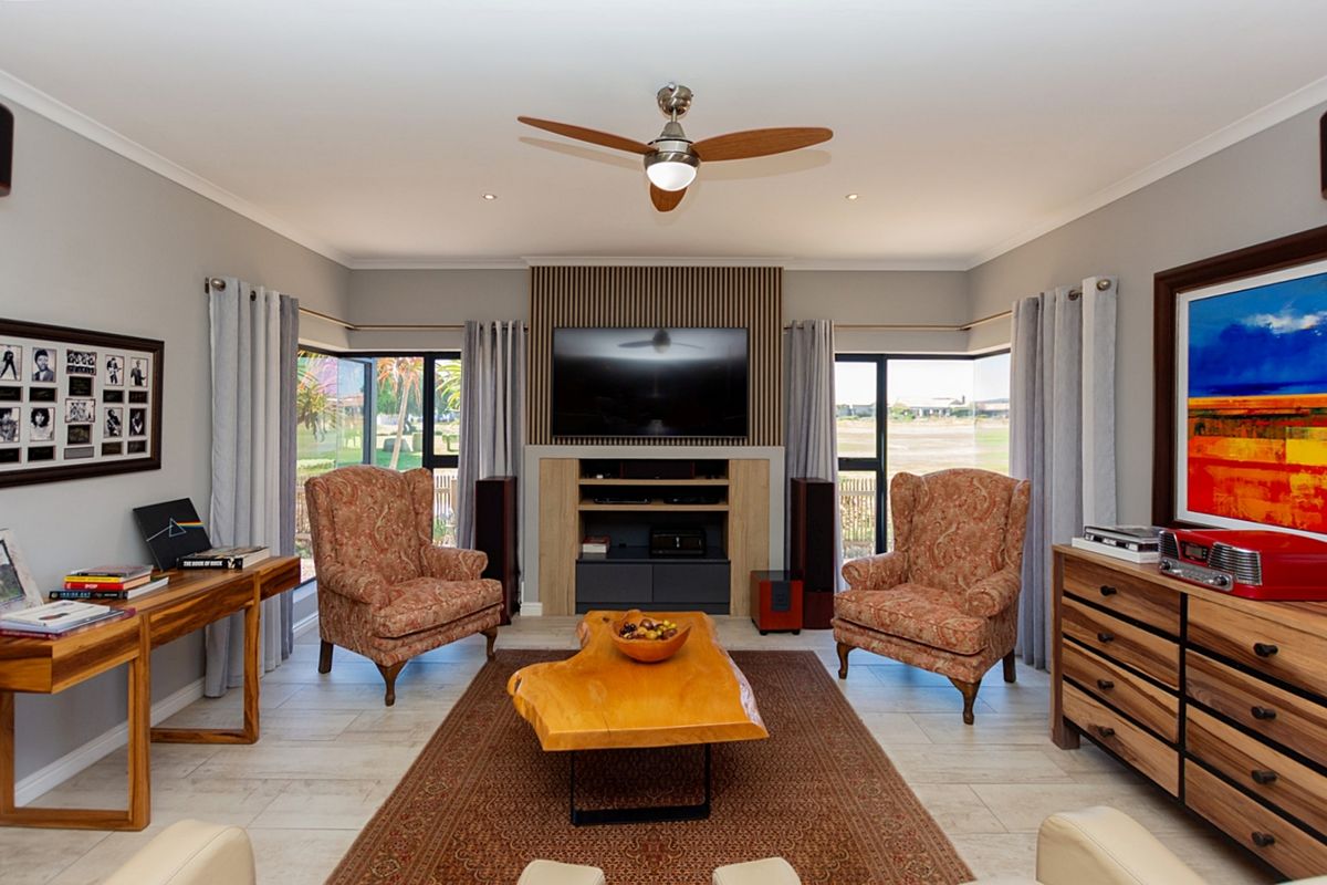 A well-maintained living room featuring a central media unit with slatted wood detailing, tiled flooring, recessed lighting, and a ceiling fan.