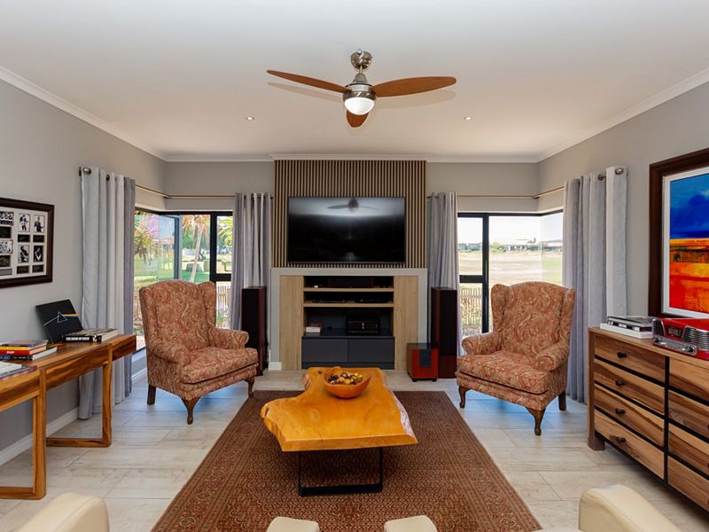 A well-maintained living room featuring a central media unit with slatted wood detailing, tiled flooring, recessed lighting, and a ceiling fan.