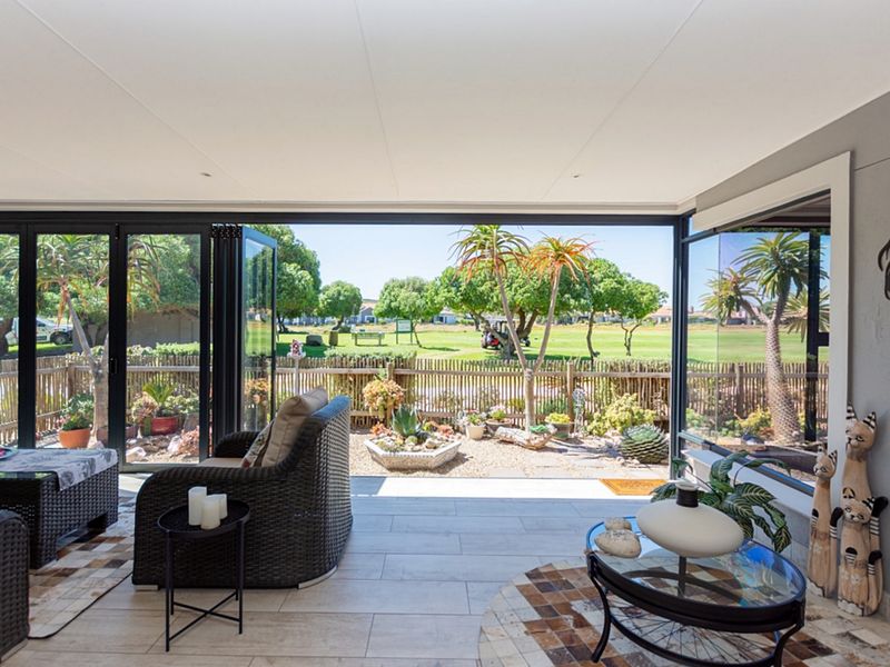 A bright, modern enclosed patio featuring large bi-fold glass doors that open to a landscaped garden and golf course view.