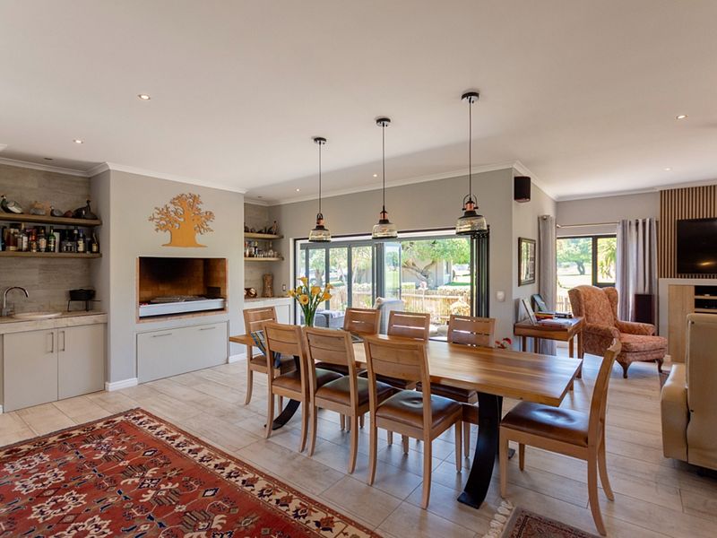 Spacious open-plan living and dining area featuring a built-in braai, modern cabinetry, tiled floors, and large sliding doors opening to the garden.