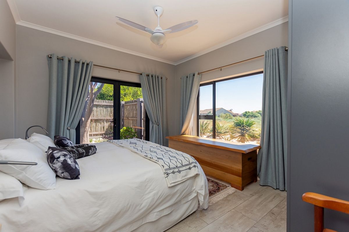 A bright and airy bedroom featuring tiled flooring, a ceiling fan, and large windows with direct access to the outdoor area.