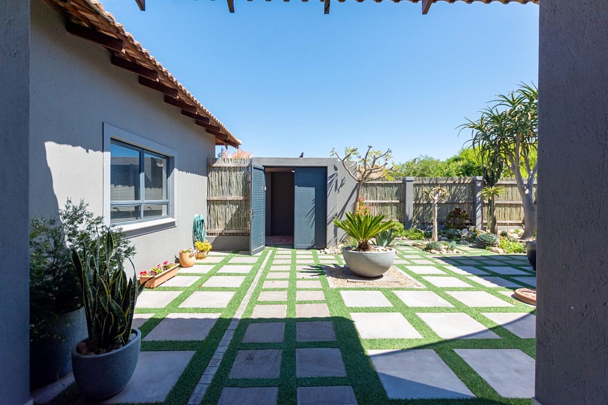 A well-maintained rear courtyard featuring paved sections with artificial grass inlay, boundary fencing, and a convenient storage shed.