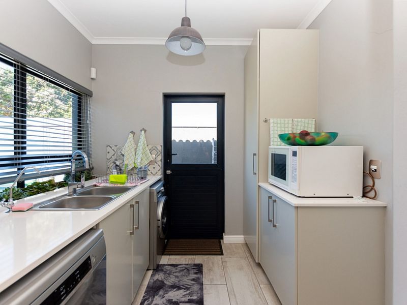 A functional laundry room featuring built-in cabinetry, a double stainless steel sink, laminate countertops, and direct access to the exterior.