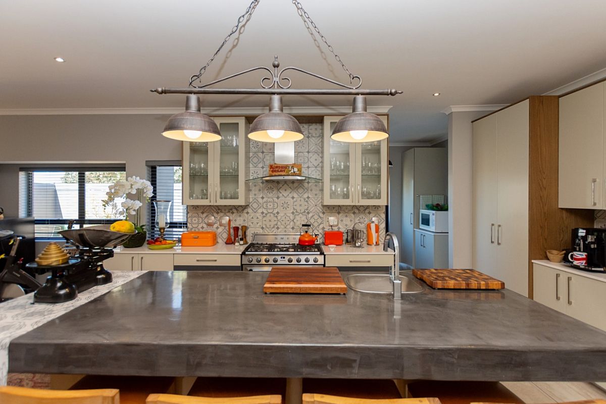 Modern kitchen featuring a large concrete island, gas stove with extractor fan, patterned tile backsplash, and ample built-in cabinetry.