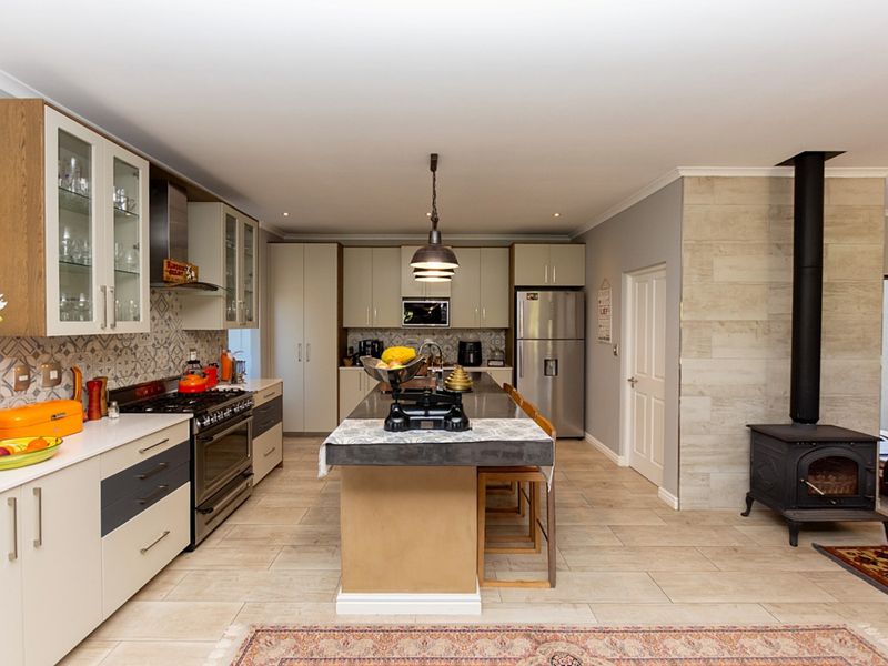 Spacious open-plan kitchen featuring a central island, modern cabinetry, gas stove, and a cozy wood-burning fireplace with a stone-clad feature wall.