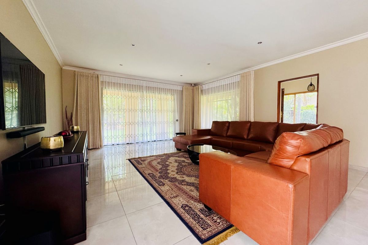 Spacious living room featuring polished porcelain floor tiles, recessed downlighting, and large sliding glass doors with security gates leading to the garden.