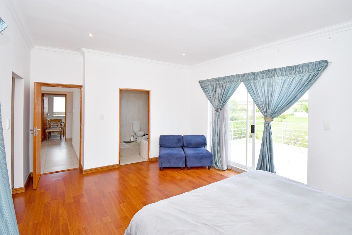 Spacious bedroom featuring laminate flooring, recessed lighting, and direct access to an en-suite bathroom and a private balcony through sliding glass doors.