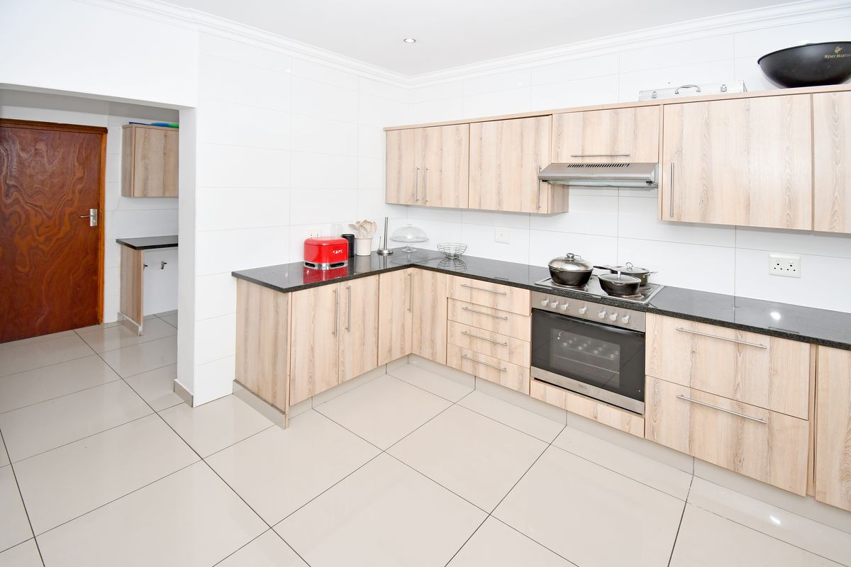 Modern kitchen featuring light wood-grain cabinetry, granite countertops, integrated oven and hob, and neutral tiled flooring with an adjacent scullery area.