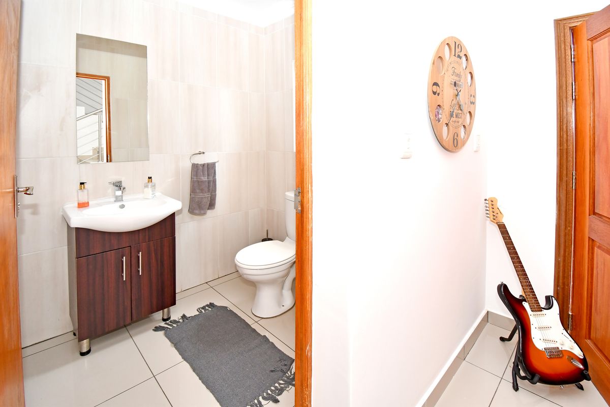A compact bathroom featuring a modern vanity cabinet, ceramic basin, wall-mounted mirror, and toilet with neutral tiled finishes.
