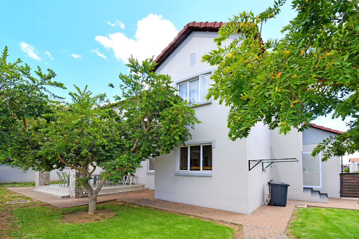 Rear view of the townhouse featuring a paved patio area, well-maintained lawn, and established trees against a clean plastered facade.
