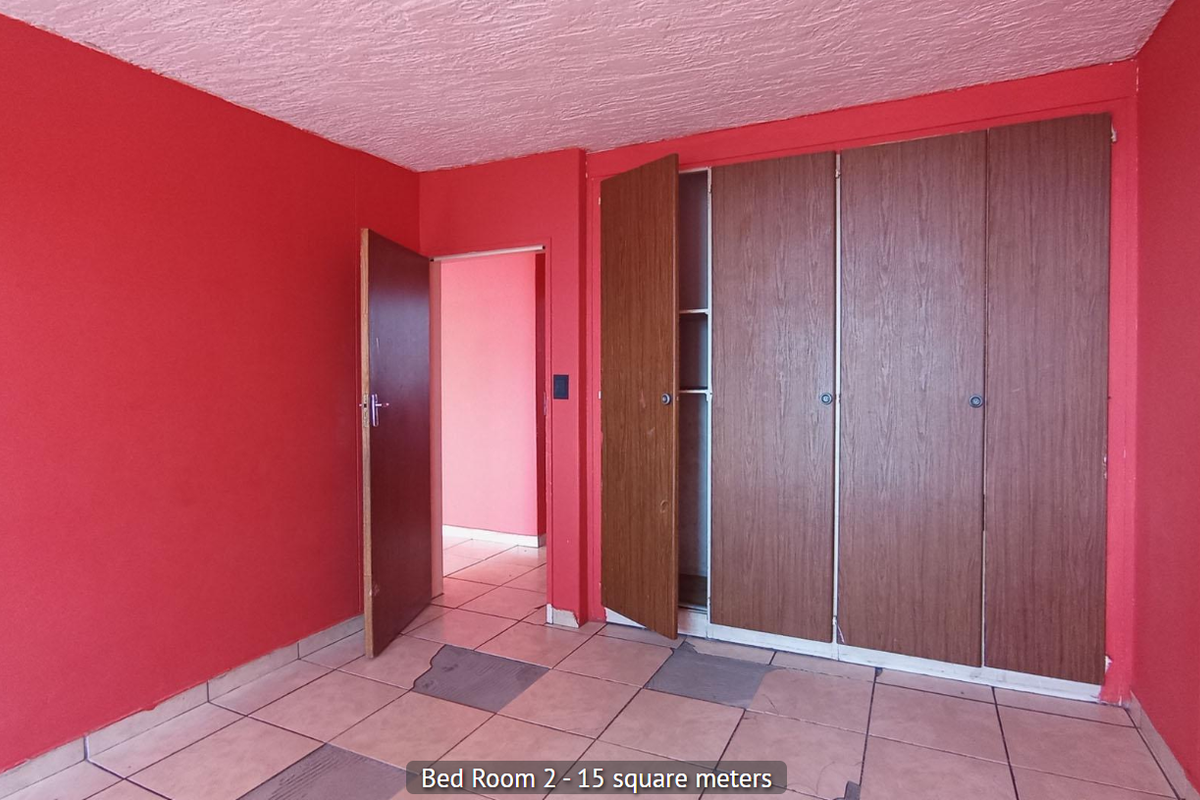An empty bedroom featuring built-in wooden cupboards, tiled flooring, and a textured ceiling, ready for renovation or restyling.