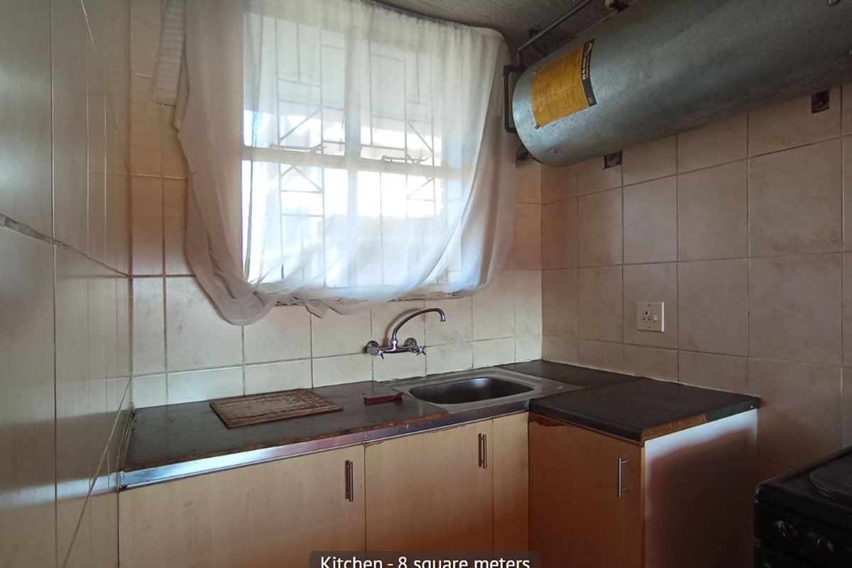 A compact kitchen featuring tiled splashbacks, laminate countertops, a stainless steel sink, and an exposed electric water heater unit.