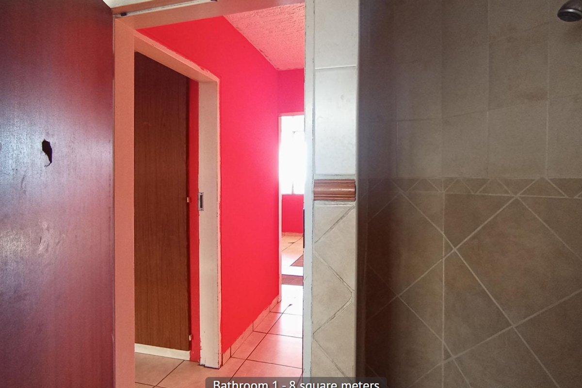 A bathroom interior featuring tiled walls and flooring with a shower head, showing signs of wear and dated finishes.